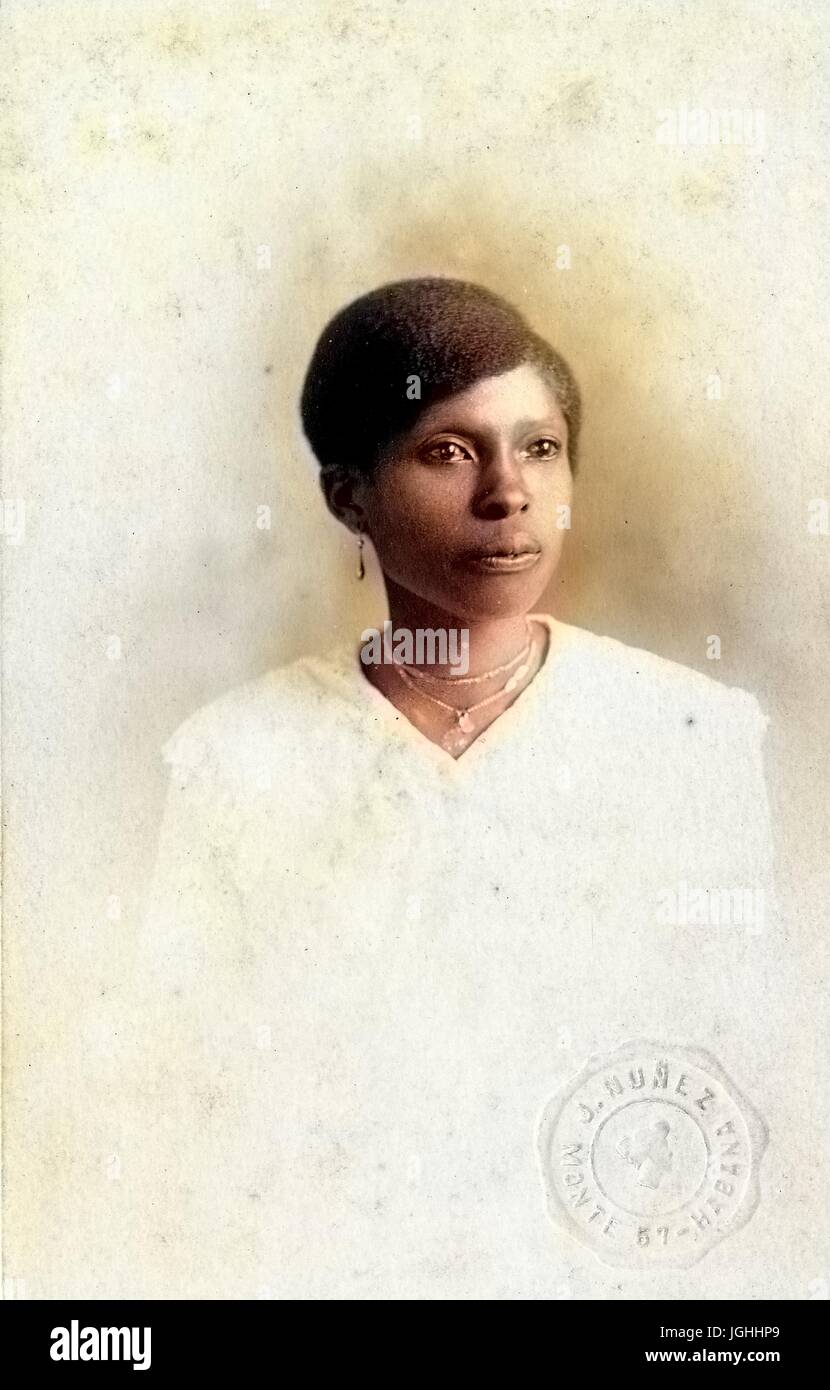 Taille bis Porträt sitzenden afroamerikanische Frau, trägt ein weißes Kleid, Halskette und Ohrringe mit einem ernsten Gesichtsausdruck, 1915. Hinweis: Bild wurde digital eingefärbt wurde mit einem modernen Verfahren. Farben können Zeit ungenau sein. Stockfoto