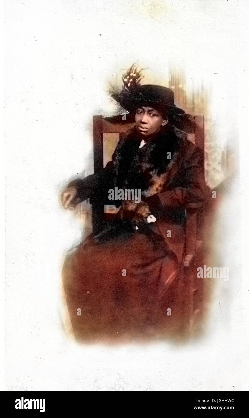 Sitzen in voller Länge Portrait von African American Milf mit einem neutralen Gesichtsausdruck trug ein dunkles Kleid, einen dunklen Mantel und ein Hut mit Federn, 1915. Hinweis: Bild wurde digital eingefärbt wurde mit einem modernen Verfahren. Farben können Zeit ungenau sein. Stockfoto