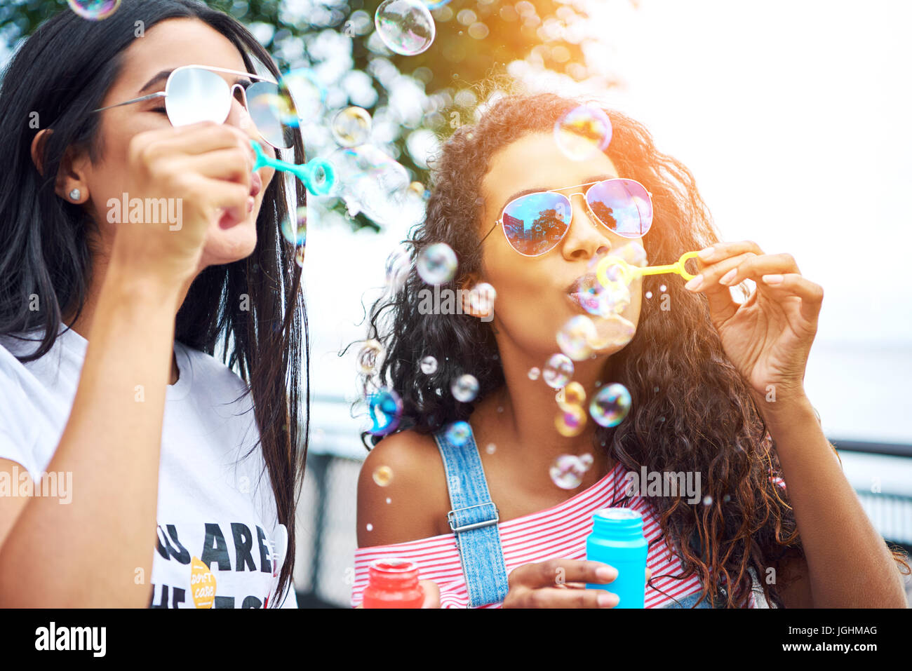 Zwei unbeschwerte junge Freundinnen Spaß zusammen mit einem Spielzeug Blase Wand sprudelt weht, genießen einen sonnigen Tag zusammen draußen Stockfoto