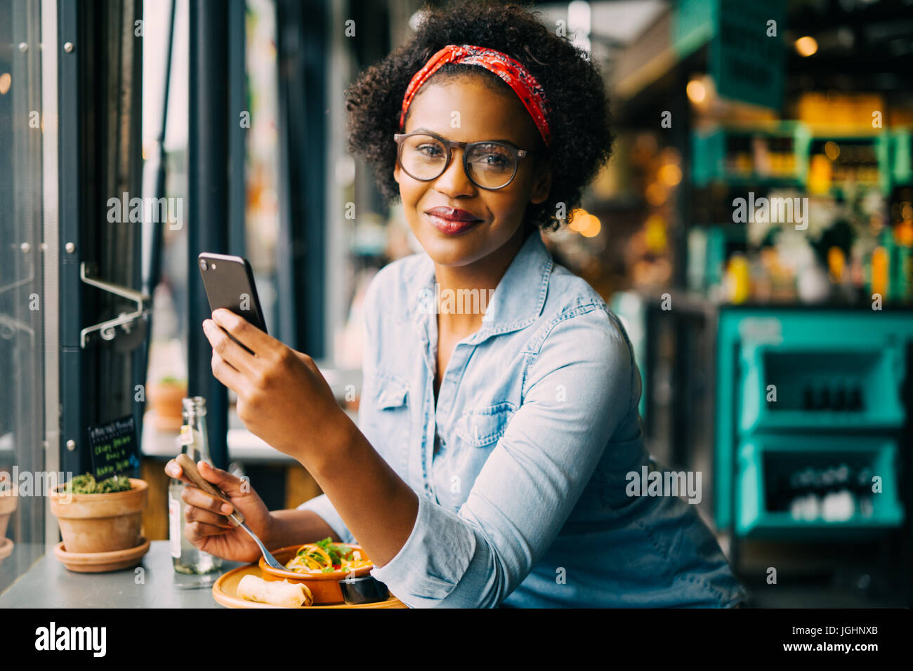 Lächelnde junge afrikanische Frau SMS auf ein Handy zu lesen, während saß allein an einem Schalter in einem Café genießen Sie eine Mahlzeit Stockfoto