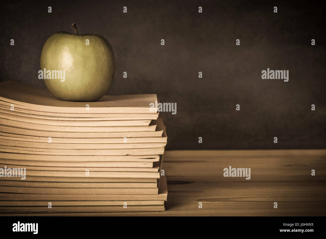 Vintage-Stil Bild eines Lehrers Schreibtisch aus Holz mit einem Apfel auf einem Haufen von gebrauchte, getragene, Schulhefte.  Tafel in soft-Fokus-Hintergrund.  U Stockfoto