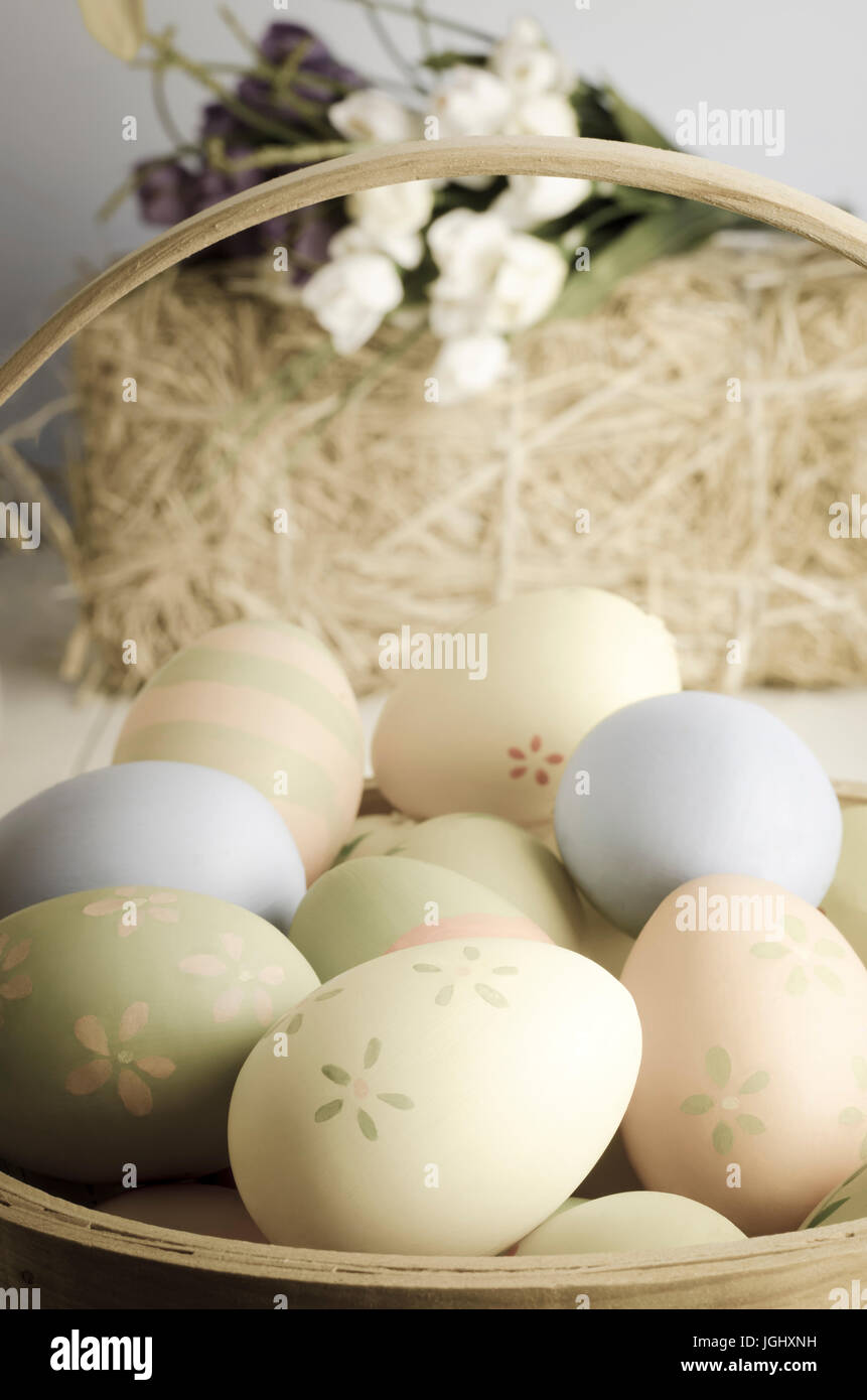 Eine Auswahl an verzierte Ostereier in einem Weidenkorb auf einem Tisch, mit Strohballen und Krokusse im Hintergrund. Stockfoto