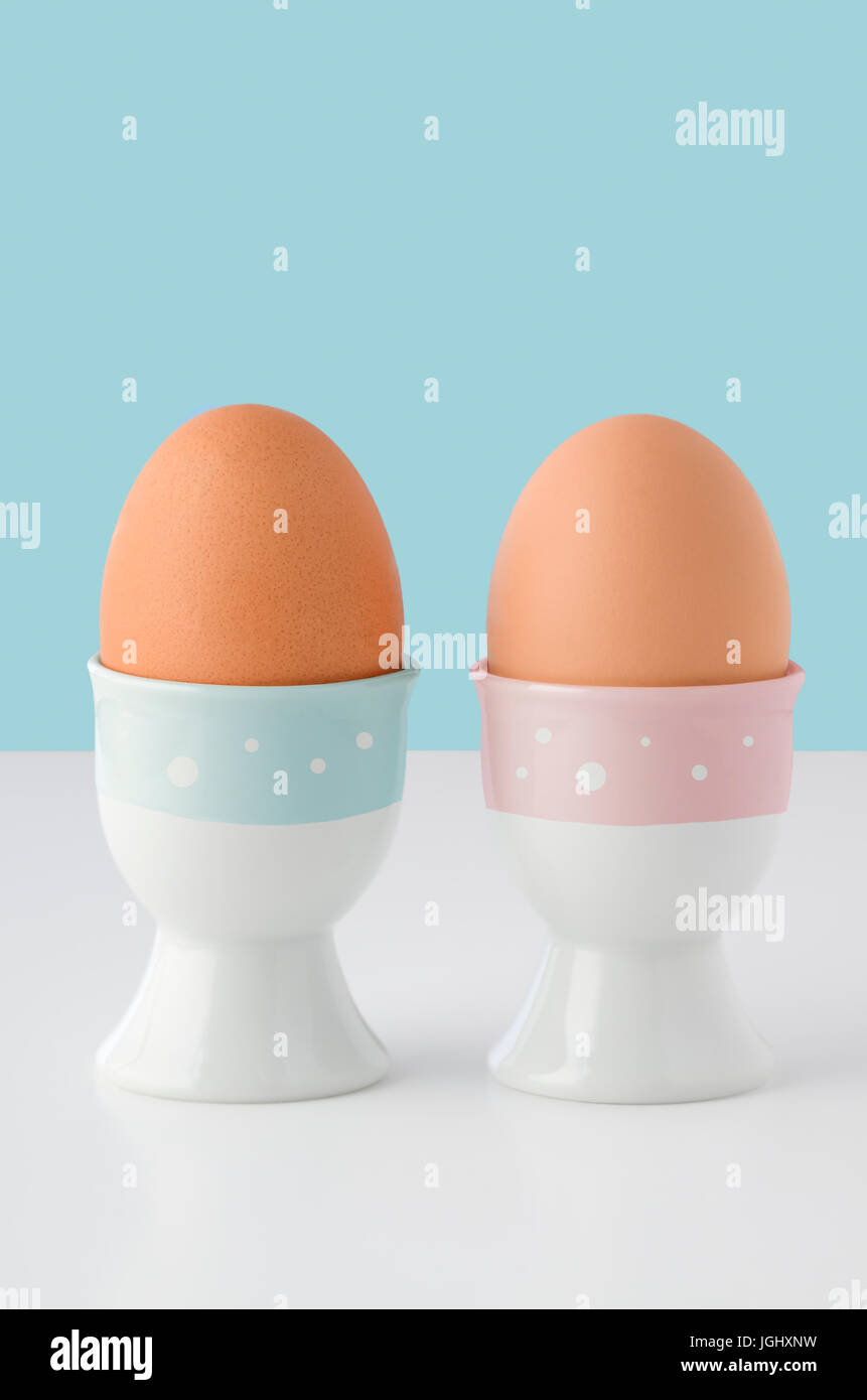 Zwei Eierbecher, dekoriert mit rosa und blauen Streifen mit weißen Flecken und Holding braunen Eiern auf weißen Tisch mit hellblauem Hintergrund.  Raum-Abov kopieren Stockfoto