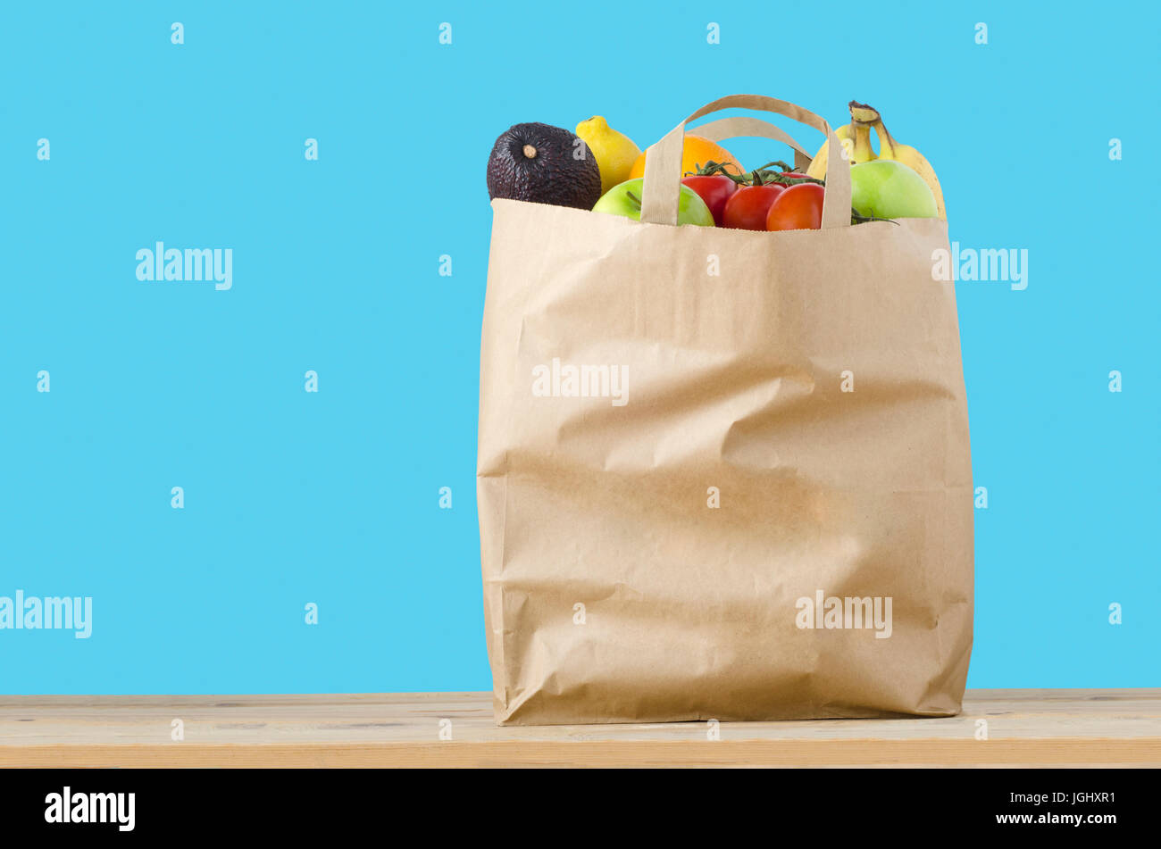 Eine braune Papiertüte Shopping, gefüllt mit Obstsorten auf einem hellen Holzoberfläche an die Spitze.  Isoliert auf türkis blauem Hintergrund. Stockfoto