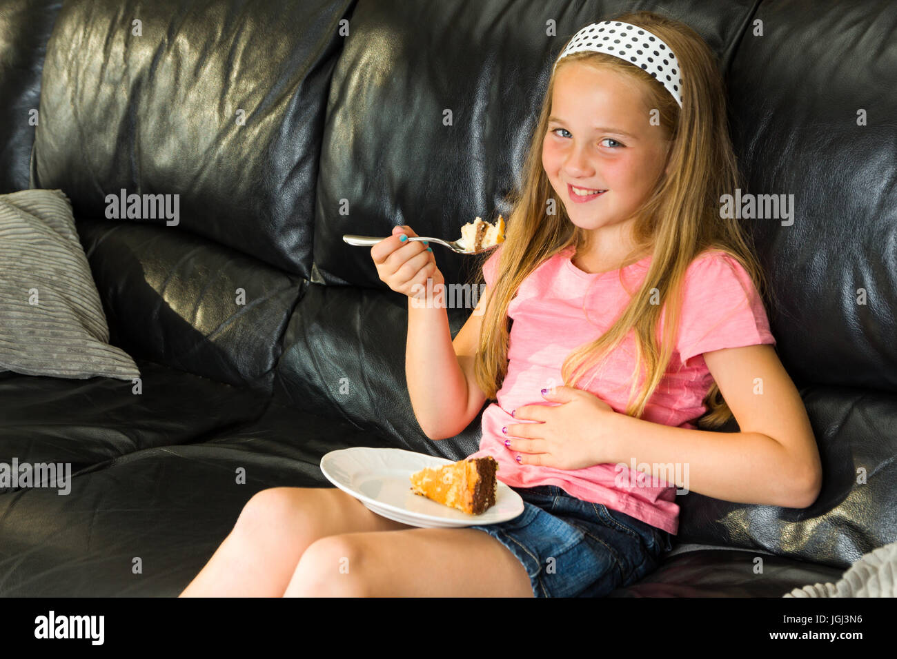 Hübsche junges Mädchen genießt Essen Dessert auf der Couch, während ihr Bauch zu berühren Stockfoto