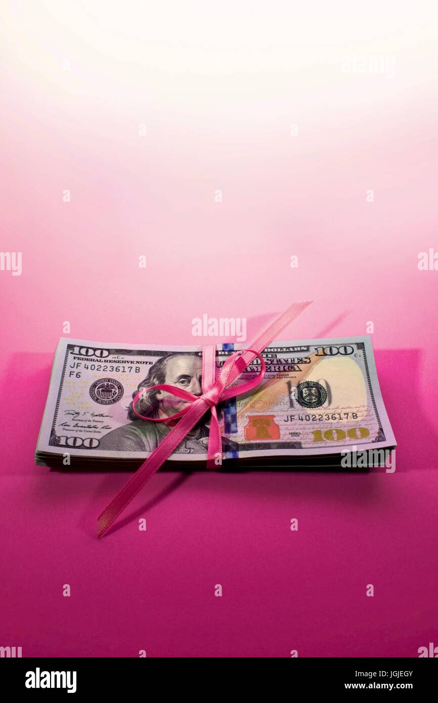 Stapel von neuen hundert-Dollar-Rechnungen Bar 100 USD amerikanisches Geld auf einem rosa Hintergrund statt, zusammen mit eine rosa Schleife gebunden in einem Bogen Stockfoto