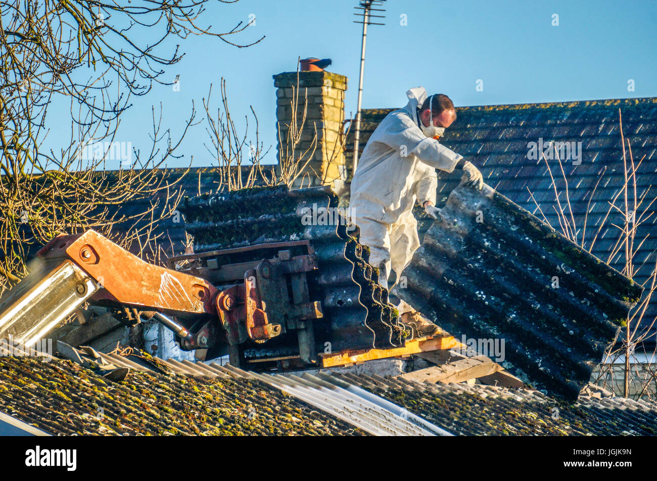 Ein Mann durch das Tragen von schützender Kleidung während der Entfernung von Asbest Dacheindeckung aus einer alten Scheune. Lincolnshire, England, UK. Stockfoto