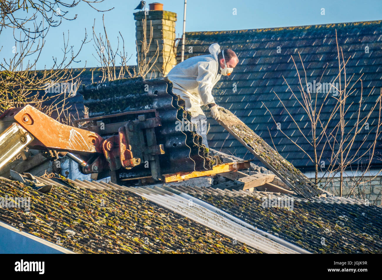 Ein Mann durch das Tragen von schützender Kleidung während der Entfernung von Asbest Dacheindeckung aus einer alten Scheune. Lincolnshire, England, UK. Stockfoto