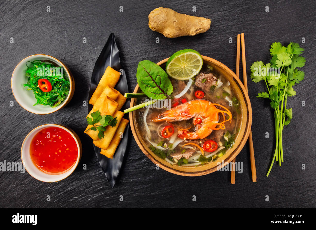 Asiatische Suppe Pho Bo mit Frühlingsrollen, Ansicht von oben auf schwarzem Stein serviert. Stockfoto