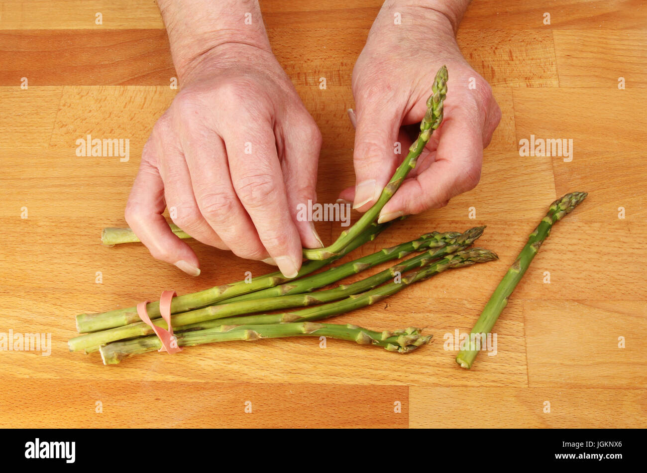 Zwei männliche Hände Vorbereitung Spargelstangen auf einem hölzernen Küchenarbeitsplatte Stockfoto