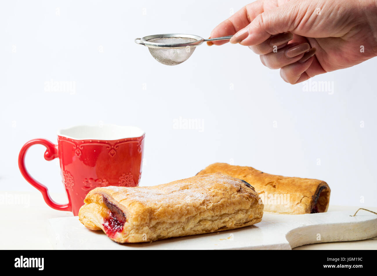 Weibliche Hand Zugabe von Zucker um Blätterteig-Gebäck vor weißem Hintergrund Stockfoto Weibliche Hand Zugabe von Zucker um Blätterteig-Gebäck vor weißem Hintergrund Stockfoto