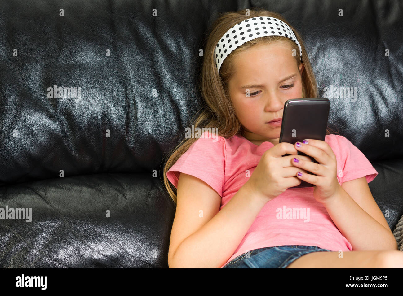 Hübsches kleines Mädchen mit Smartphone auf der couch Stockfoto