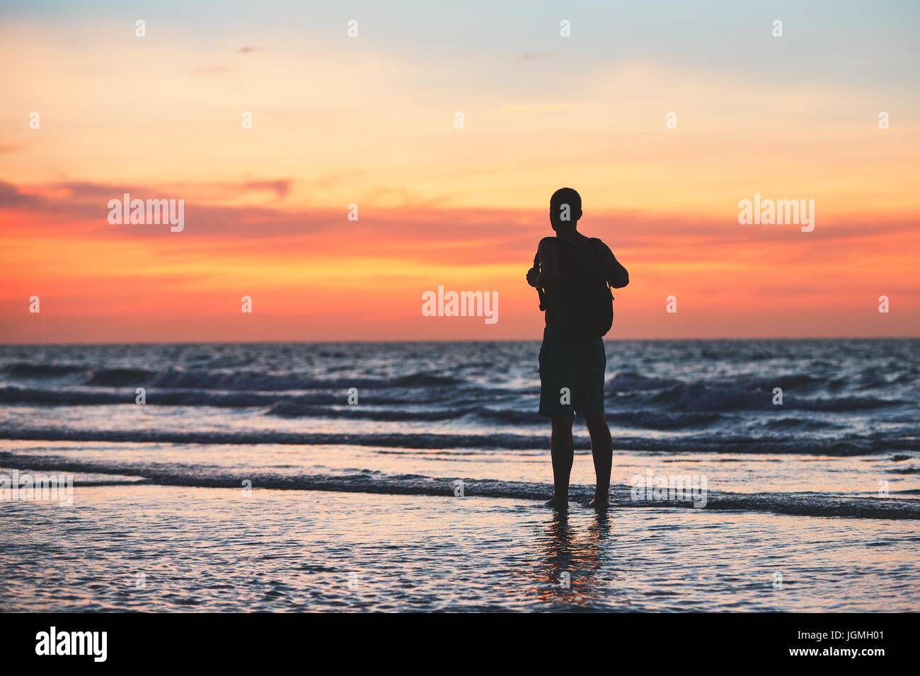 Kontemplation am tropischen Strand. Nachdenklicher Mann (Tourist) im Wasser des Meeres bei Sonnenuntergang steht. Stockfoto