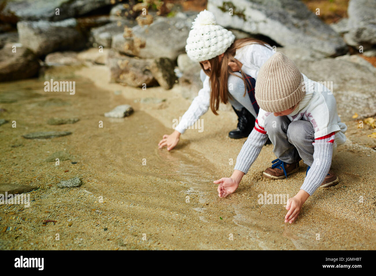 Kinder spielen im Freien in der Natur: sitzen am Ufer des Sees berühren Sand im klaren Wasser an warmen Herbsttag Stockfoto