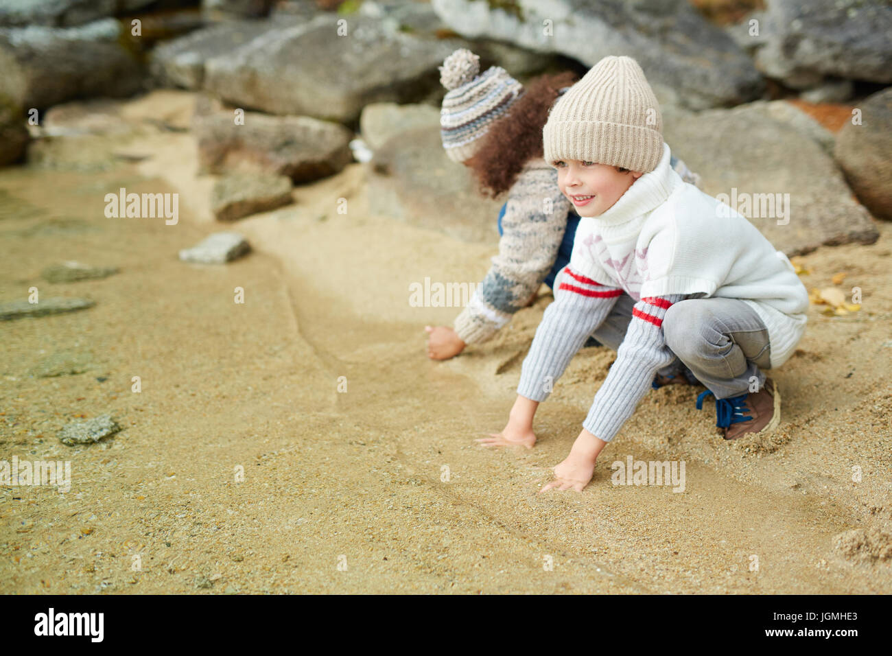 Niedlicher kleine Junge sitzt auf sandige Seeufer durch klares Wasser Stockfoto