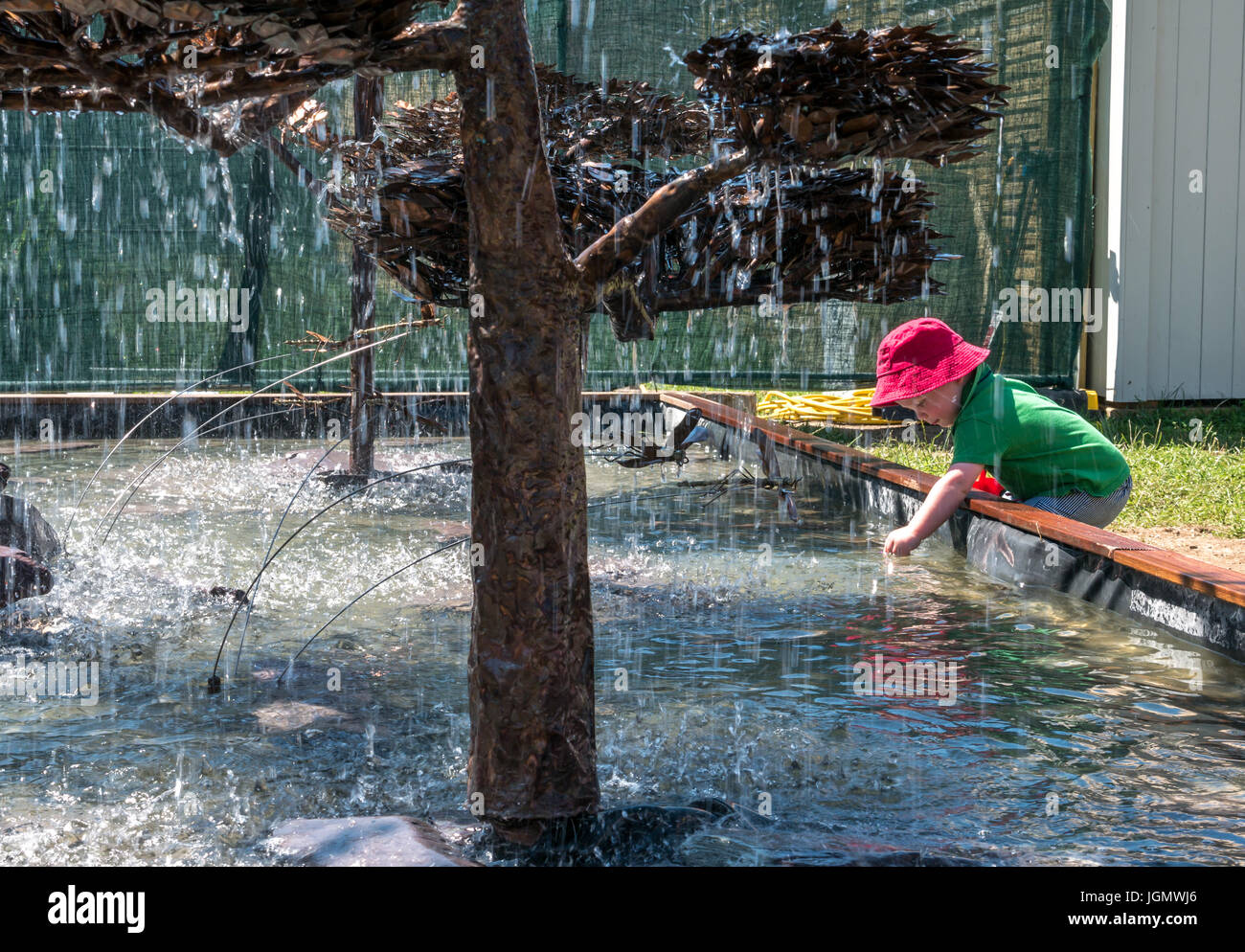 Kleines Kind mit rotem Sonnenhut, das sich in das Wasser des Wasserbrunnens lehnt, auf der RHS Hampton Court Flower Show, London, England, Großbritannien Stockfoto