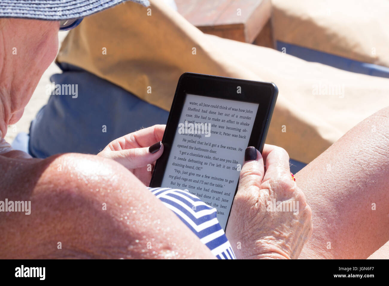 Ältere Frau liest Kindle Ebook an einem Strand in der Sonne Stockfoto