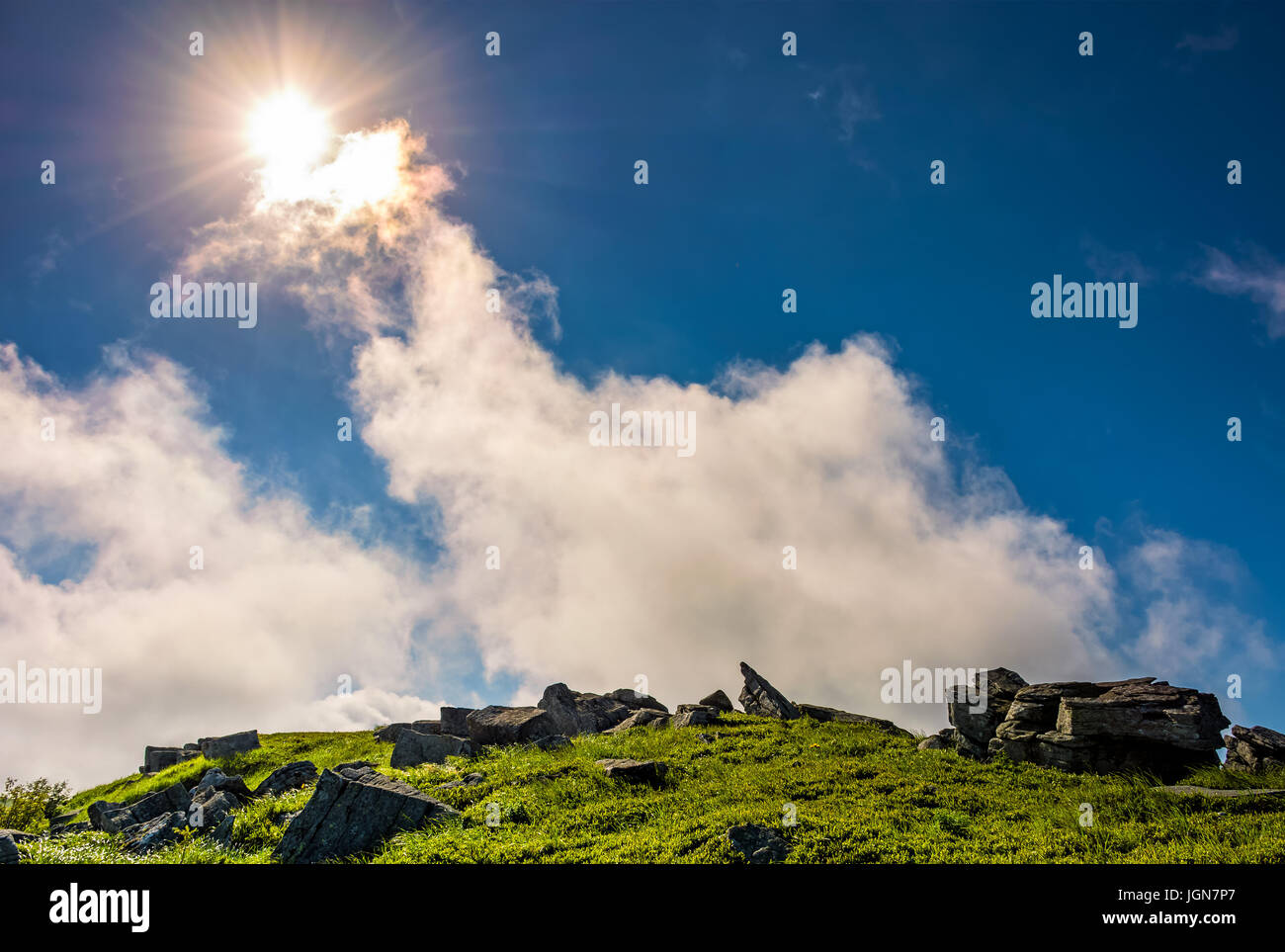 Sunburst auf einem blauen Himmel mit Wolken über den Bergen mit felsigen Hügel Stockfoto