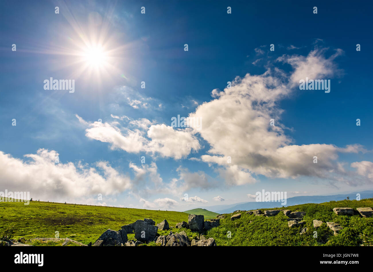 Sunburst auf einem blauen Himmel mit Wolken über den Bergen mit felsigen Hügel Stockfoto