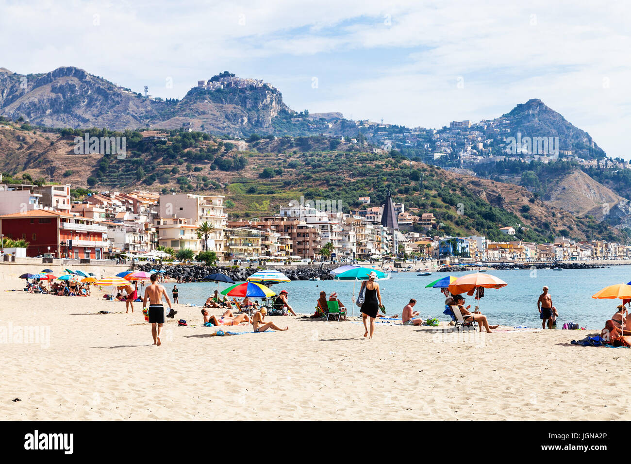 GIARDINI NAXOS, Italien - 28. Juni 2017: Urlauber am Sandstrand in Giardini-Naxos-Stadt und Blick auf Taormina Stadt am Kap. Giardini Naxos ist am Meer r Stockfoto