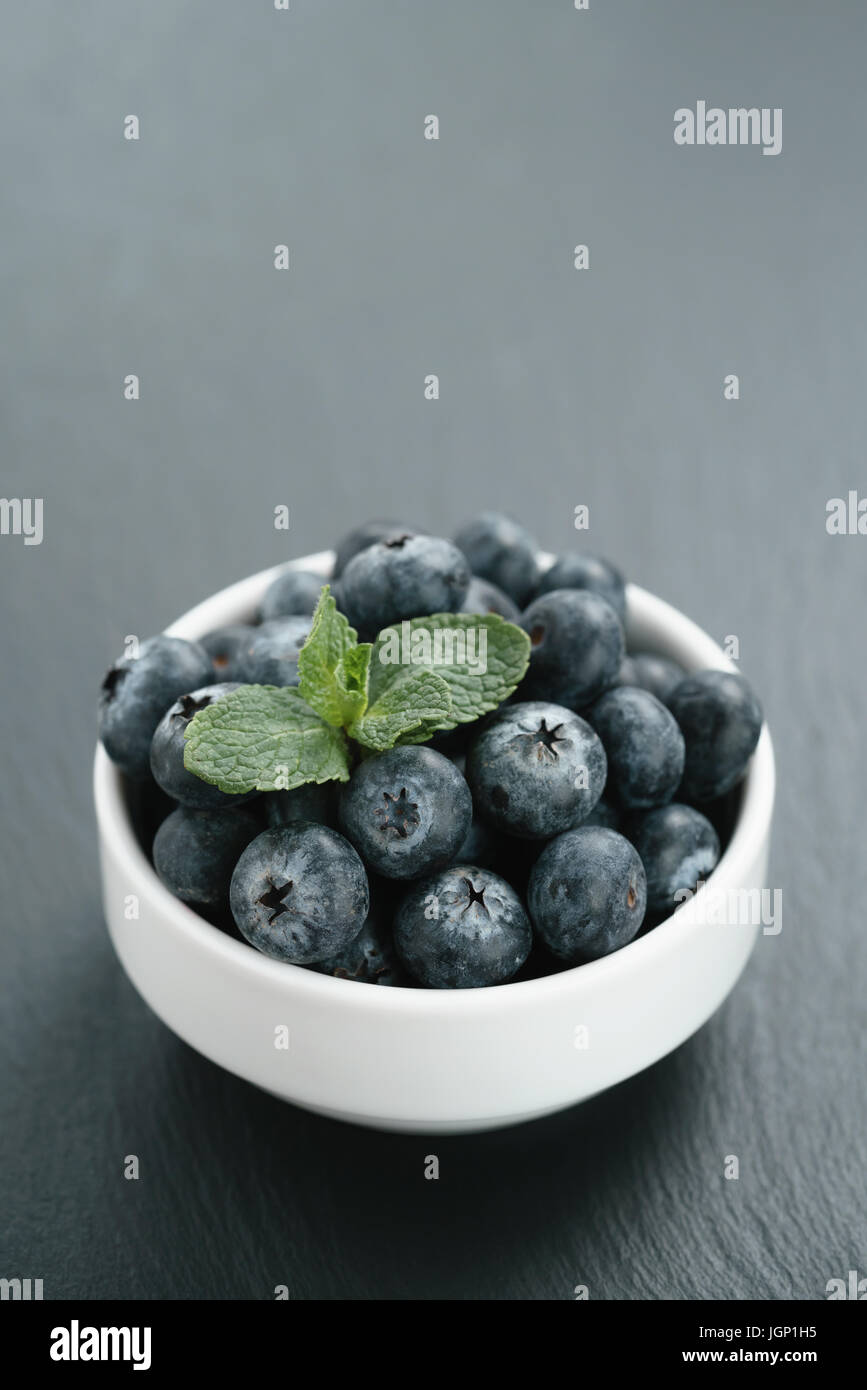 frische Heidelbeeren mit Minze Blätter in weiße Schüssel auf Schiefer board Stockfoto