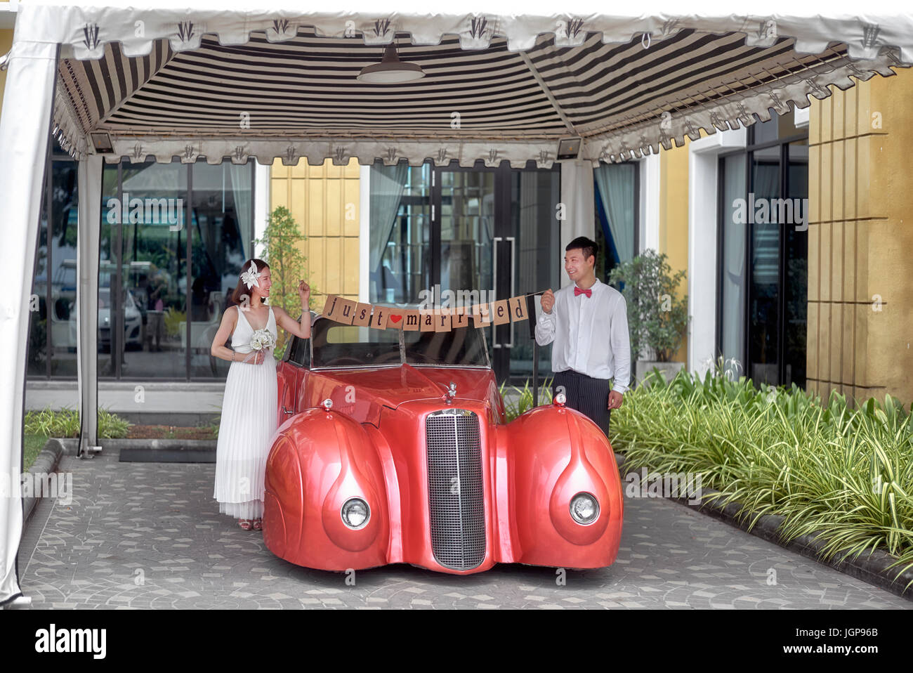 Frisch verheiratetes junges Paar posieren für Hochzeitsfotos neben einem Cadillac Auto. Thailand-Südostasien Stockfoto