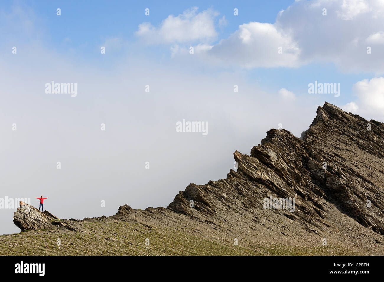 Frau im roten Jacke stehen am Rande des Berges mit Nebel im Hintergrund, Col Agnel, Frankreich. Stockfoto