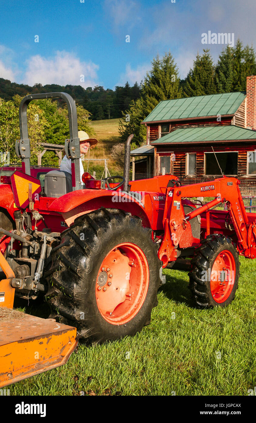 20er Jahre Bäuerin auf roten Traktor, Bauernhaus im Hintergrund Stockfoto