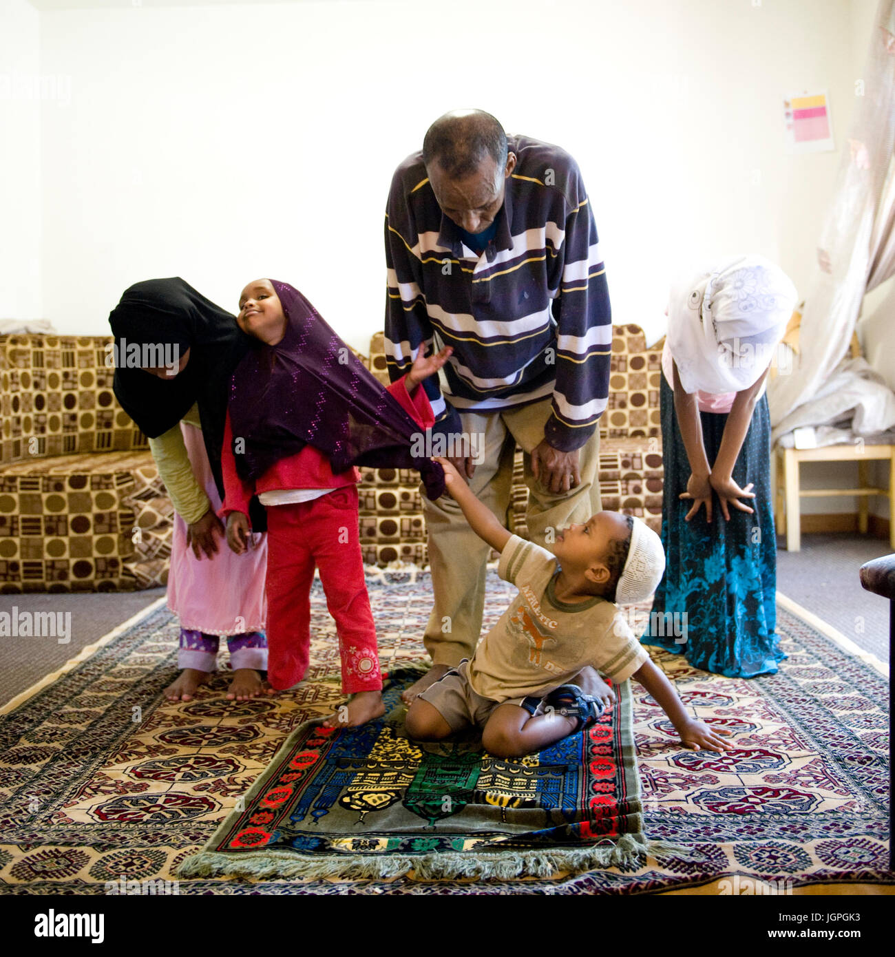 Somalische Flüchtlingsfamilie in ihr neues Zuhause in Portland, Oregon - ein kleiner Junge packt seine Schwestern Hijab während der muslimischen Gebet in der Familie. Stockfoto