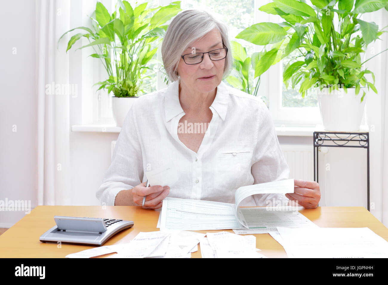 Hochrangige deutsche Frau zu Hause mit Rechner und viele Rechnungen und Quittungen, das Ausfüllen der Vordrucke der jährlichen Steuererklärung Stockfoto