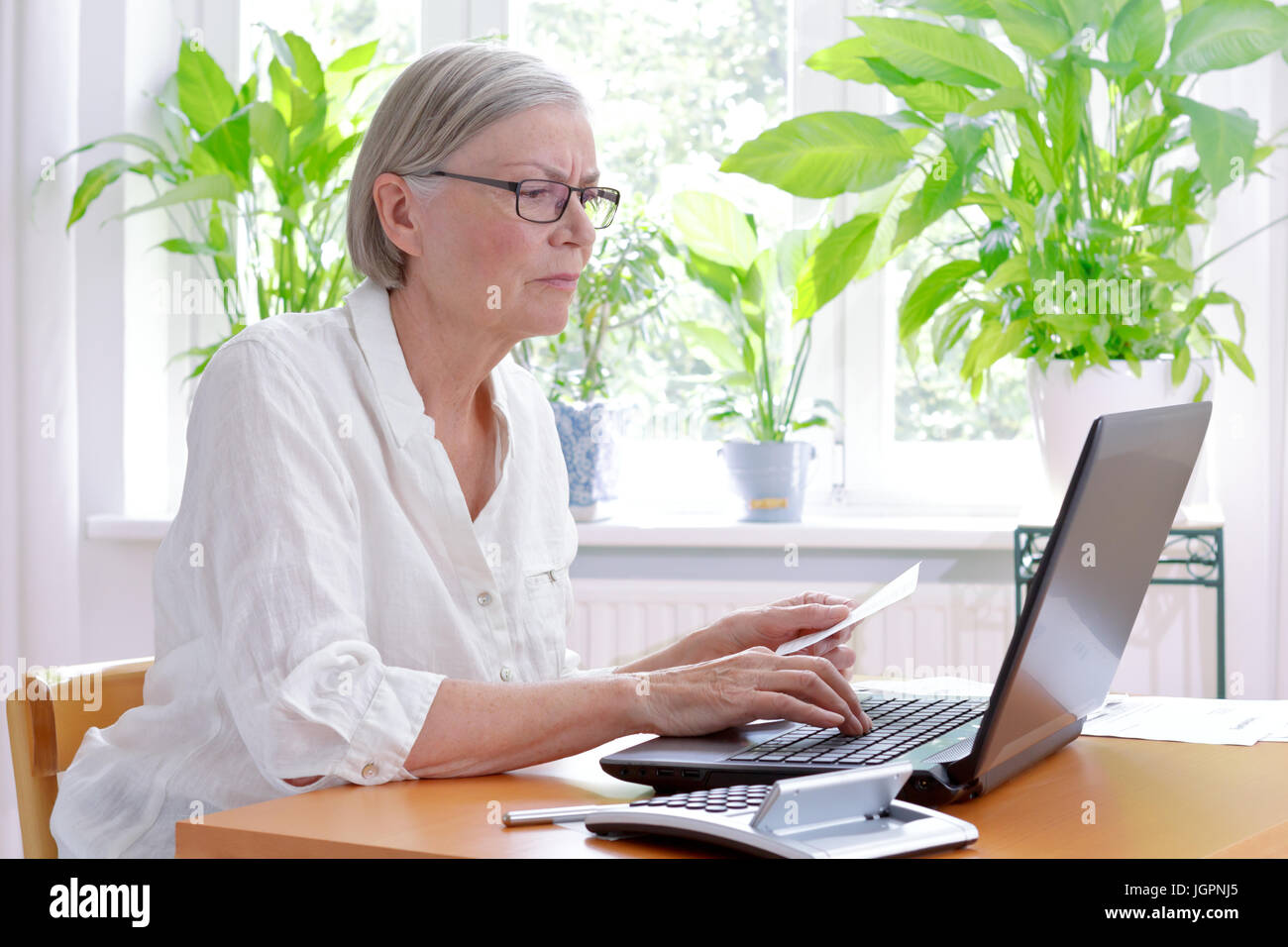 Verärgert senior Frau zu Hause mit einem Taschenrechner und viele Belege vor ihrem Laptop machen ihre jährliche Steuererklärung Stockfoto