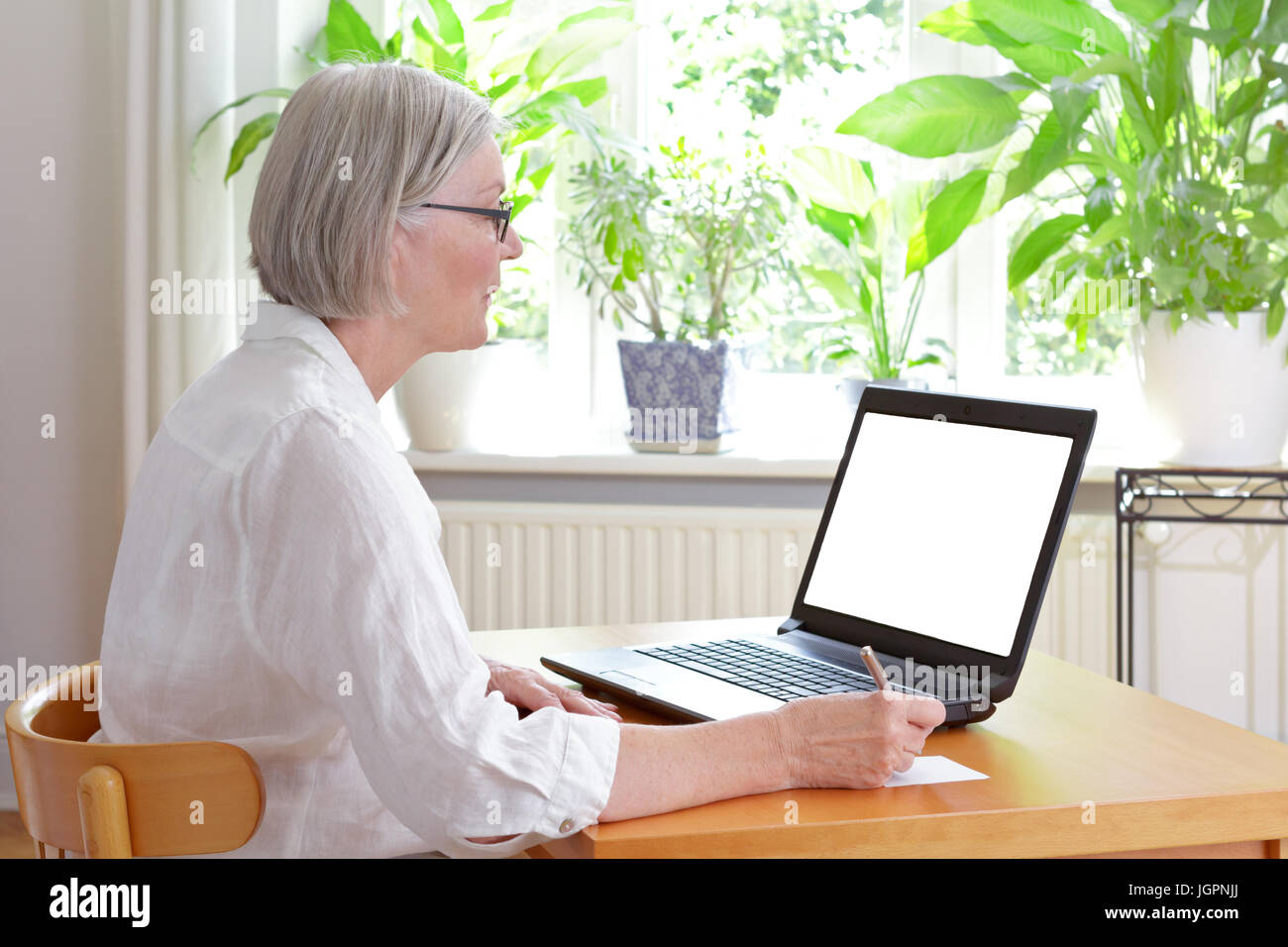 Ältere Frau zu Hause vor ihrem Laptop Notizen, online Beratung oder e-Learning - Konzept Vorlage, weißer Bildschirm, Kopie Raum Stockfoto