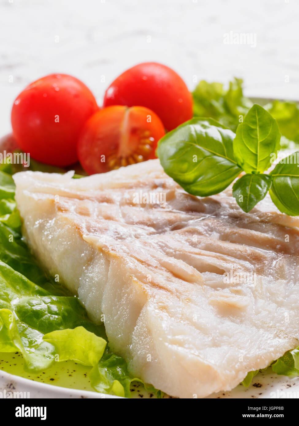 Nahaufnahme der gegrillte Kabeljau mit Basilikum und Kirschtomaten in trendigen weißen Teller. Stockfoto