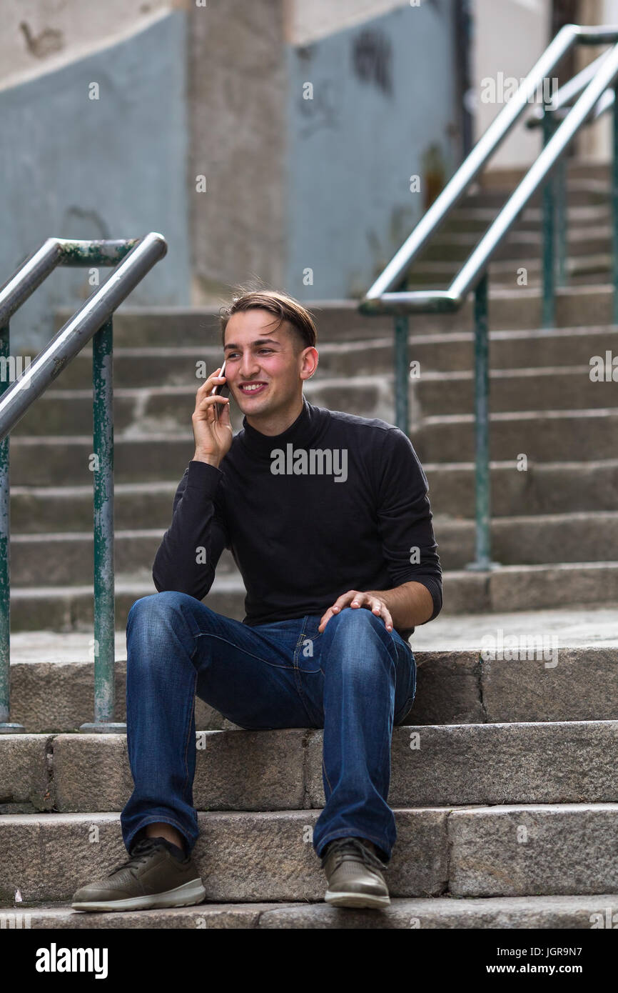 Junger Mann sitzt auf Außentreppen am Telefon zu sprechen. Stockfoto