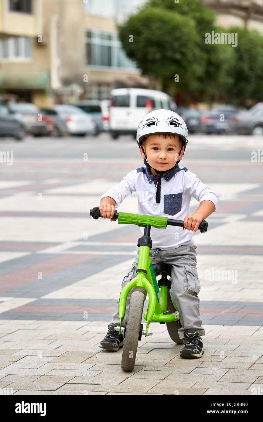 Kind Junge im weißen Helm auf seinem ersten Fahrrad mit Helm fahren. Fahrrad ohne Pedale. Stockfoto