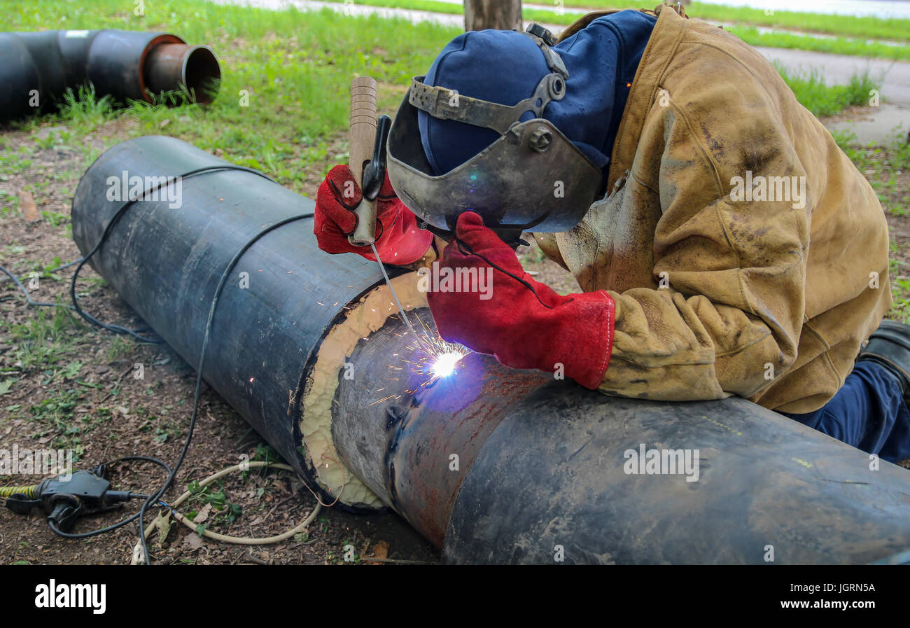 Schweißer mit Schutzausrüstung Schweißen im Freien. Arbeiter Schweißen Metall-Rohrleitungen. Stockfoto