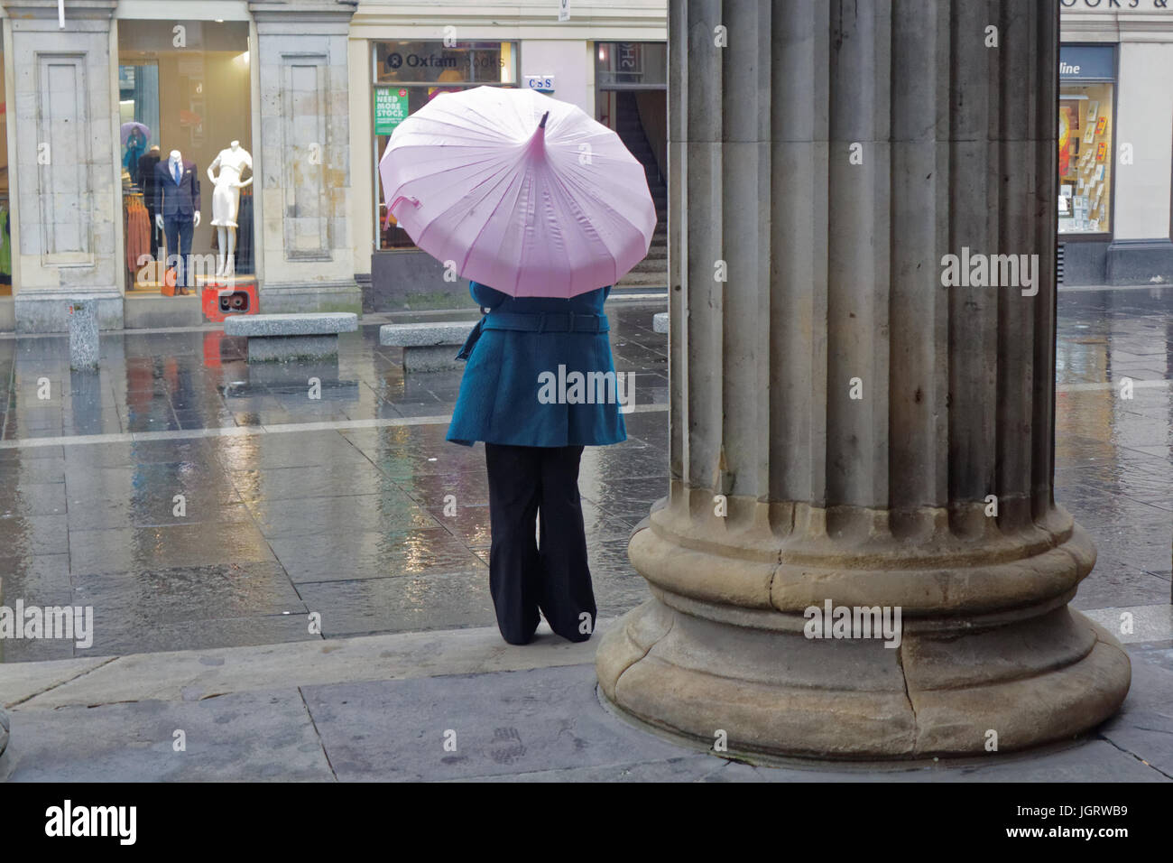 junges Mädchen Teenager Regen in Glasgow mit rosa Regenschirm Sonnenschirm auf die Straße nass Regen Tag neben Spalte brollie Stockfoto