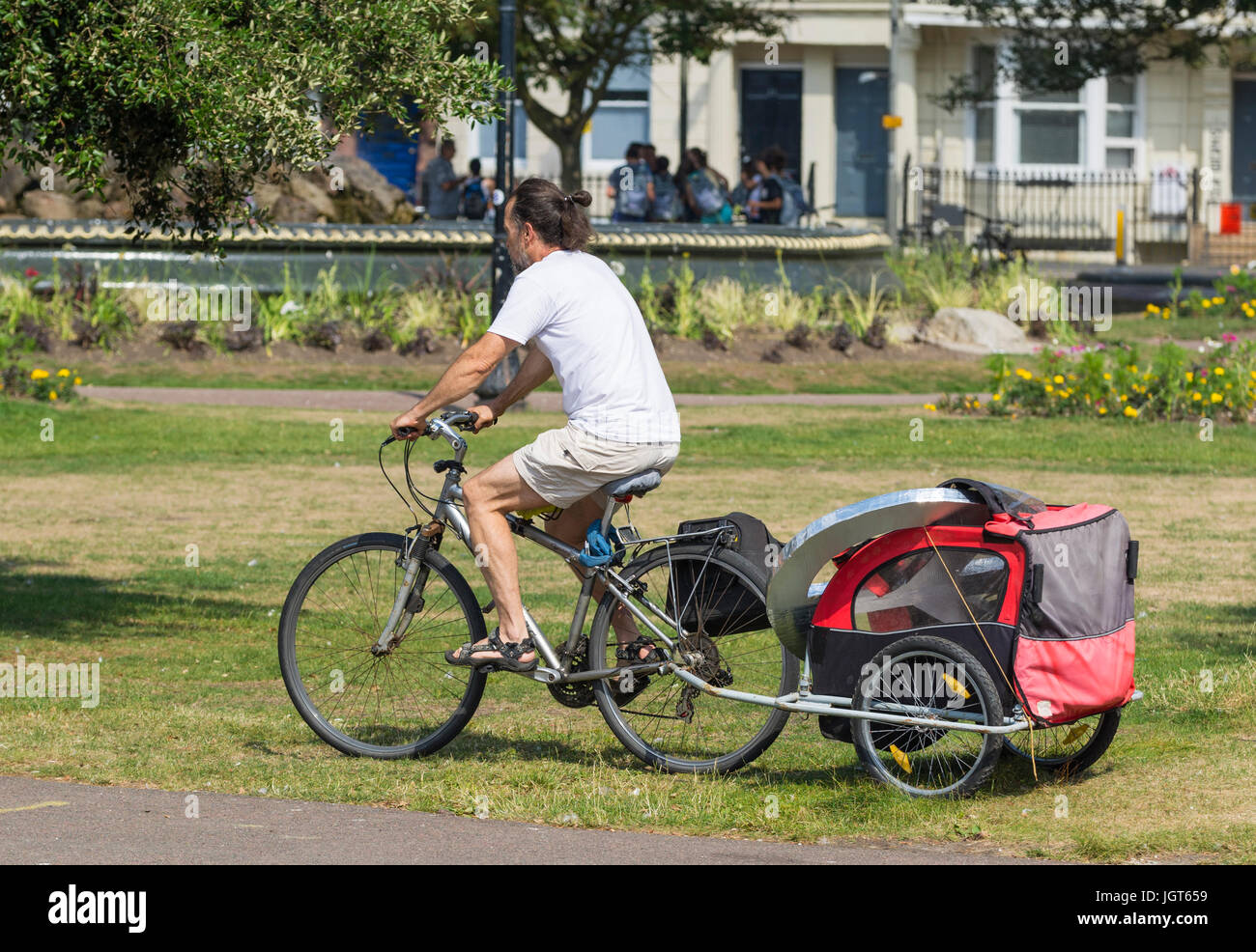 Schleppen einen Kinderwagen für ein Kind hinter seinem Fahrrad Radfahrer. Stockfoto