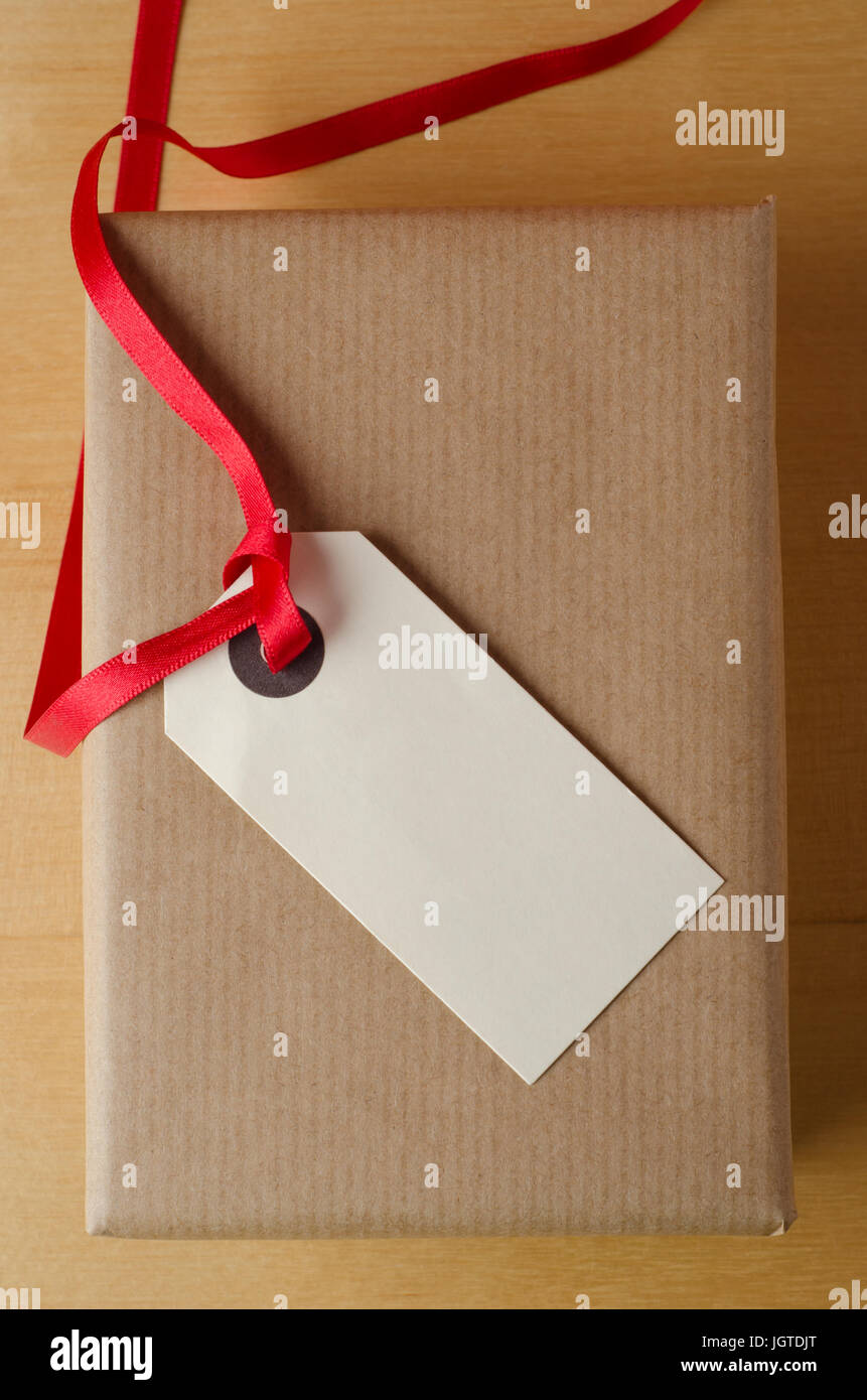 Overhead Schuss eine verpackte Packpapier-Geschenk-Paket auf Holzfurnier Tisch. Gekrönt mit einem Paket Tag und rotes Band, zeigt die leere Beschriftung nach oben, pr Stockfoto