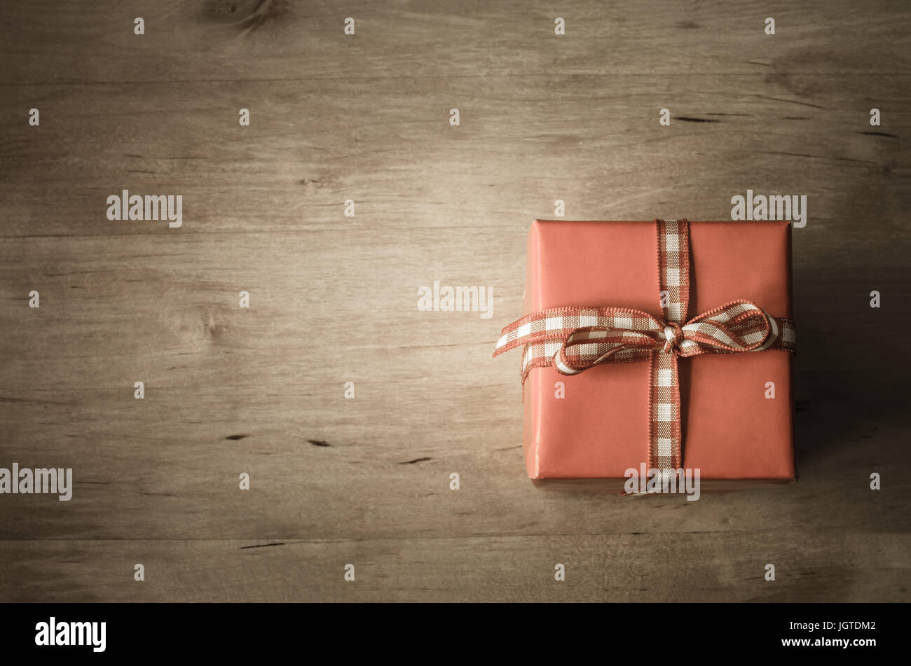 Eine quadratische Geschenkbox mit Gingham Check Band gebunden shot von oben am geplankte Holztisch.  Vintage-Stil Färbung und Vignette angewendet.  Textfreiraum Stockfoto