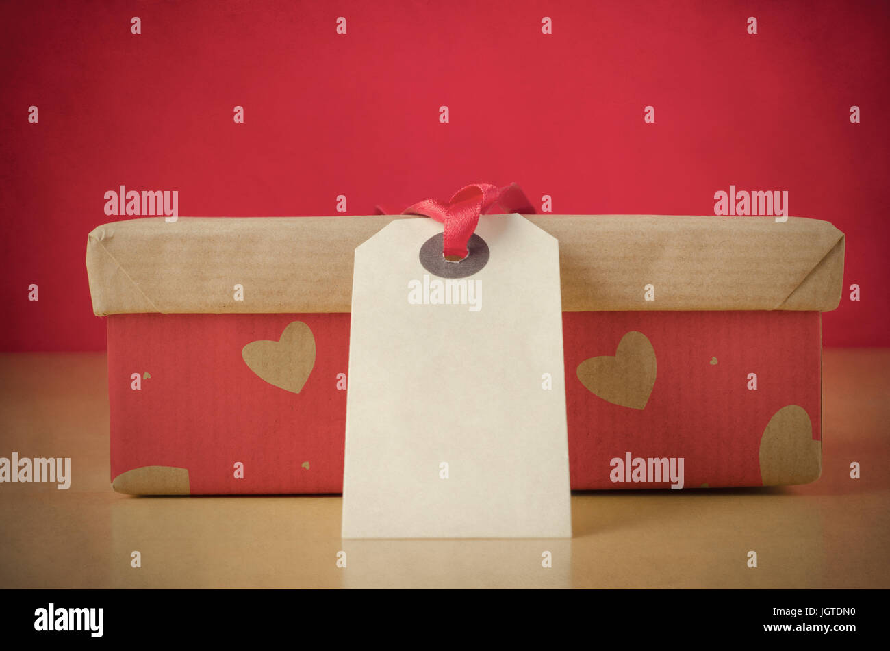 Einem geschlossenen Lidern Box mit braunem Papier Deckel und rot base auf Tisch, gemustert mit Herzformen.  Ein leeres Etikett mit rotem Band liegt gegenüber den Betrachter und l Stockfoto