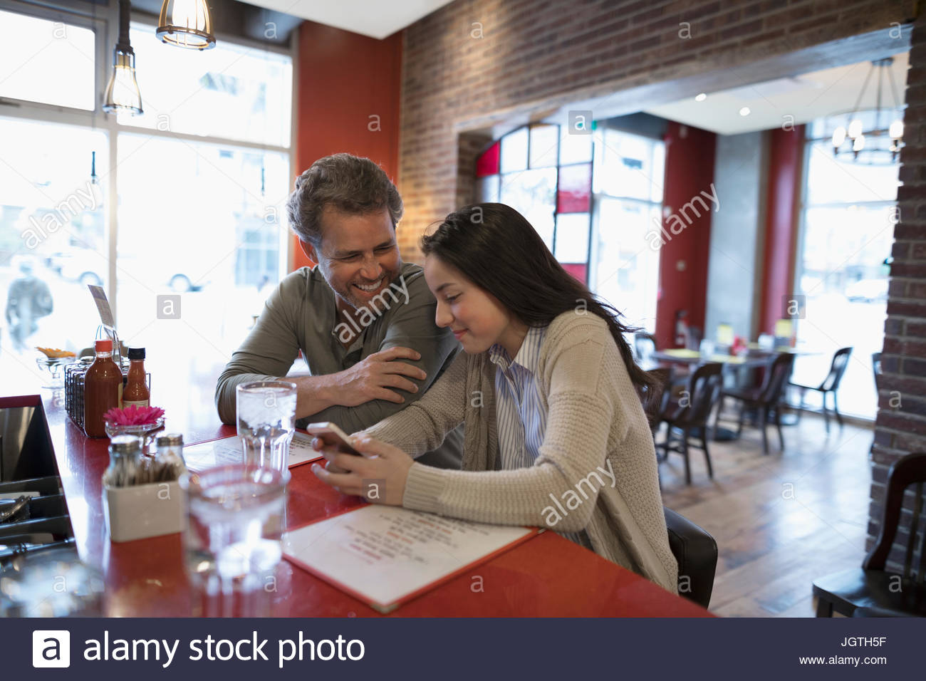 Vater und Tochter im Teenageralter mit Handy-Essen im Diner Theke Stockfoto