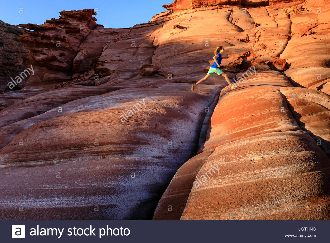 Ein Mädchen springt über Risse in einer roten Sandstein Bildung auf der Baja Halbinsel, Puerto Gato. Stockfoto