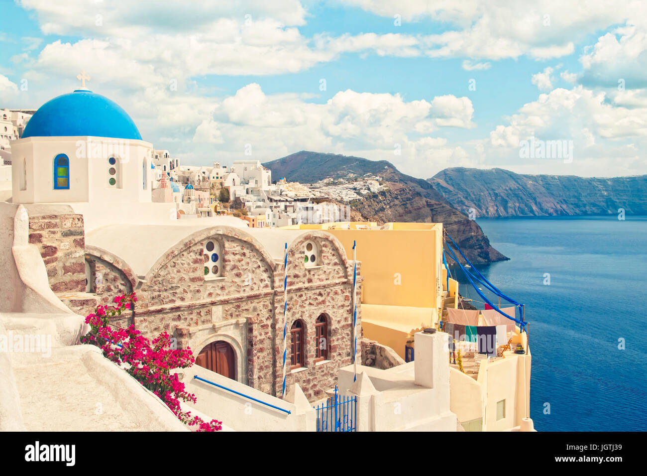 Crossen Instagram Stil Bild orthodoxen Greek church mit Blumen im Vordergrund und die Stadt mit weißen Häusern am Berg im Hintergrund, Oi Stockfoto
