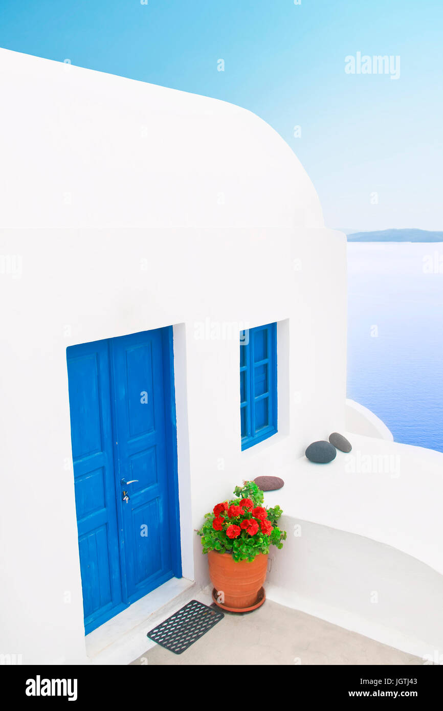 traditionellen weißen griechischen Haus mit blauen Tür-, Fenster- und Blume Topf mit roten Blüten mit wunderschönem Blick aufs Meer vor blauem Himmel, Oia, Santorini, G Stockfoto