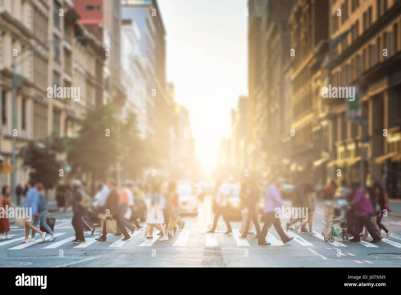 Anonyme Gruppe von Menschen zu Fuß über eine Fußgängerzone Zebrastreifen auf einer New-York-City-Straße mit einem glühenden Sonnenuntergang Licht im Hintergrund Stockfoto