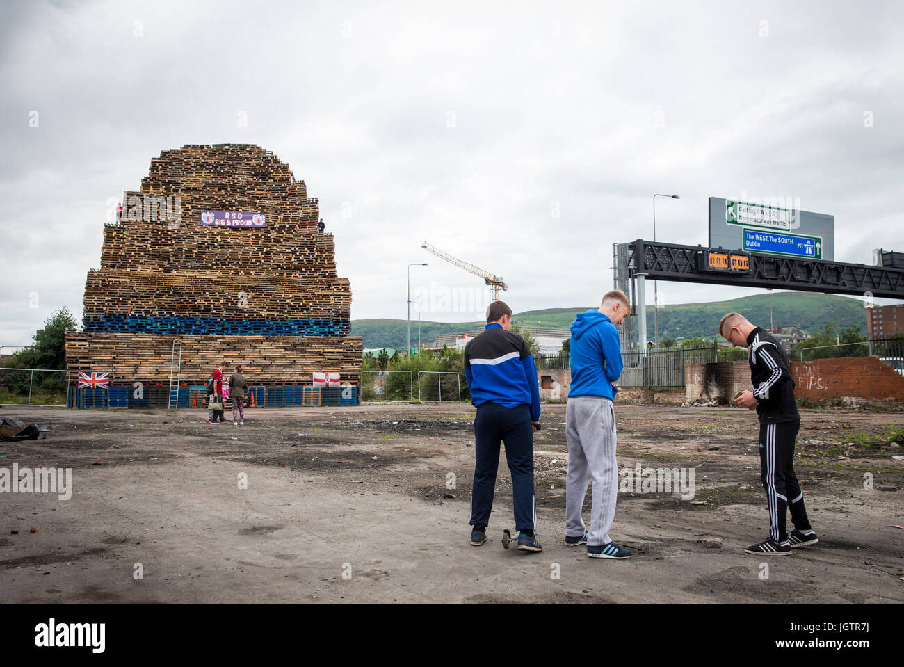 Junge Männer spielen in der Nähe von Loyalist Lagerfeuer bei Roden Street in Belfast. Polizei in Nordirland haben davor gewarnt, dass ihre Ressourcen gestreckt werden könnte, angesichts der wachsenden Angst vor Spannung um das Verbrennen der elfte Nacht Lagerfeuer. Stockfoto