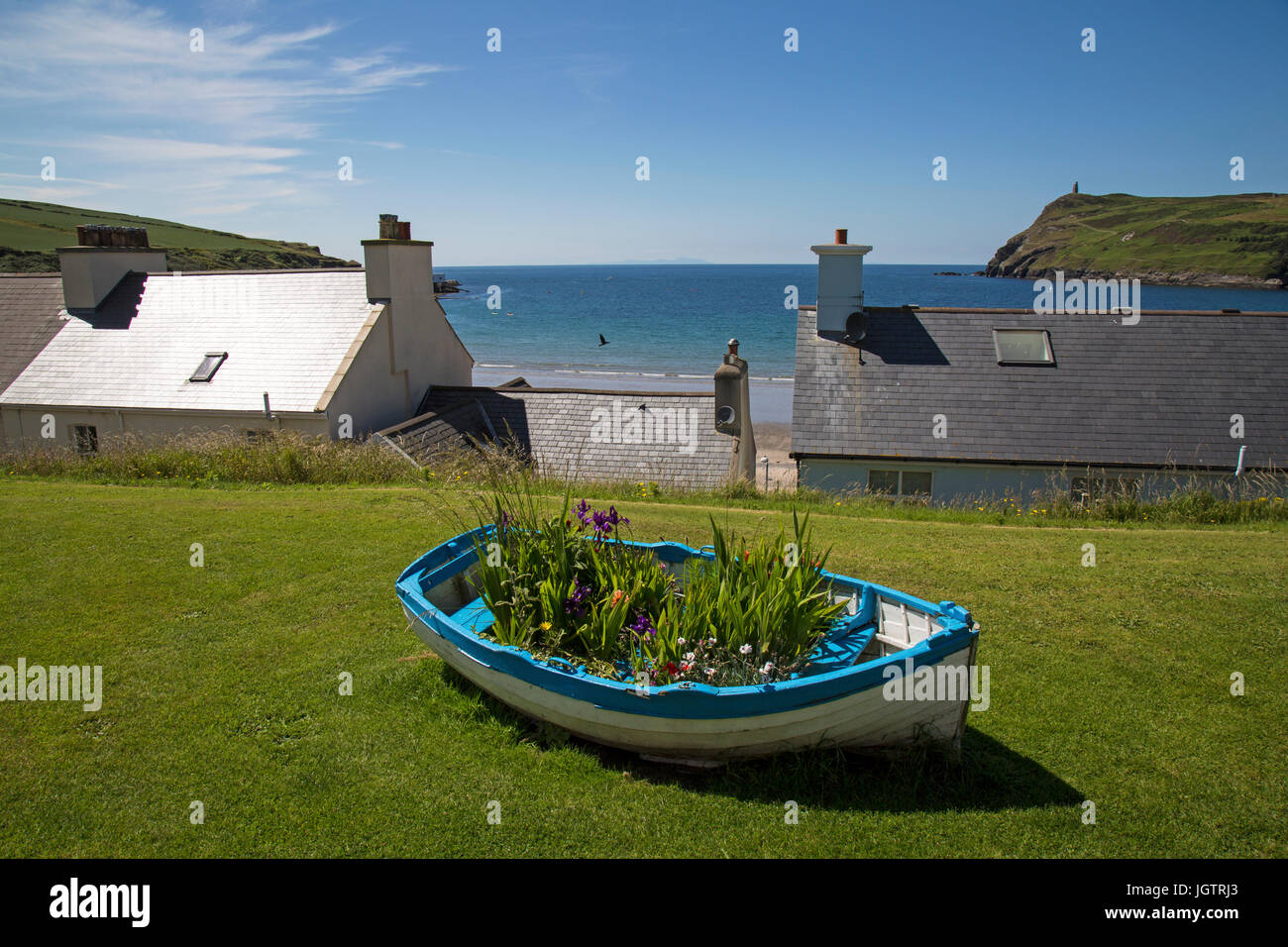 Alte Boote voller Blumen mit Blick auf Gebäude und die Bucht bei Port Erin auf der Isle of Man. Stockfoto