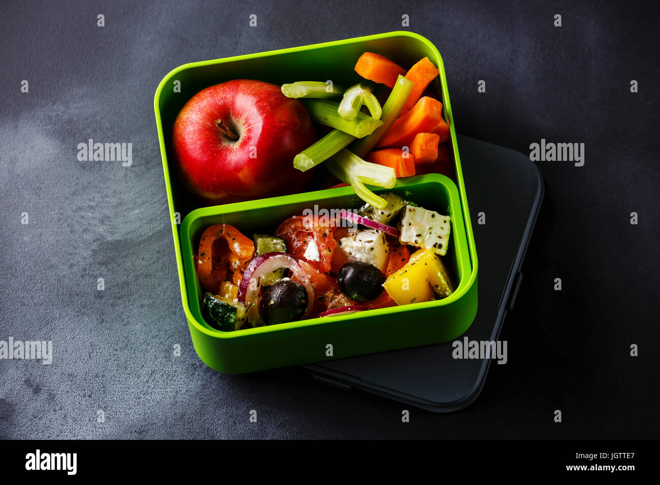 Griechischer Salat essen und Apfelfrucht in Lunchpaket auf Tafel Hintergrund herausnehmen Stockfoto