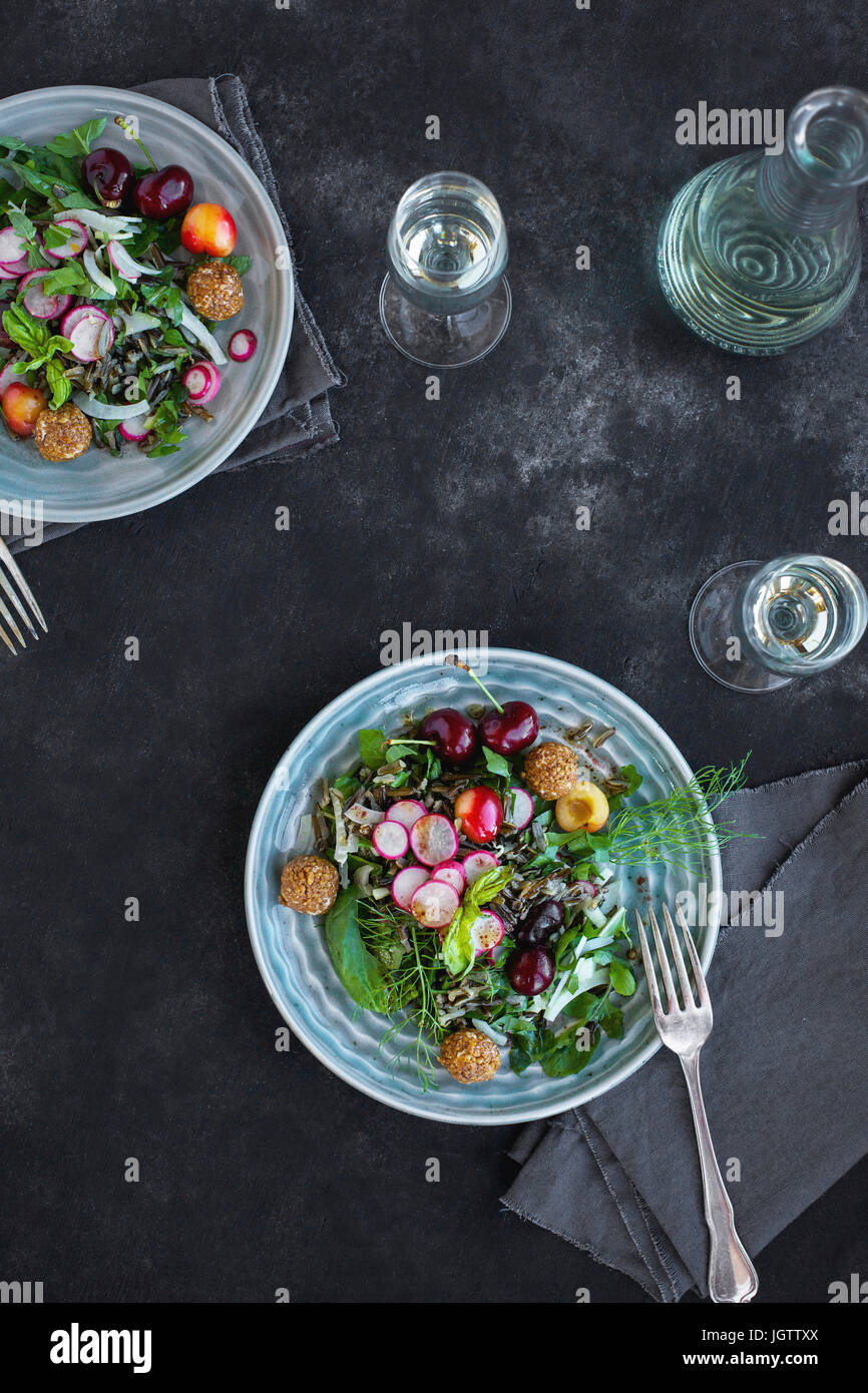 Kirsche Wildreis-Salat mit Hibiskus-Vinaigrette serviert mit Weißwein.  Auf schwarz/grau Hintergrund fotografiert. Stockfoto